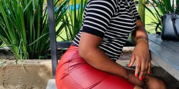 Peris, a sugar mummy in Rongai, seated outdoors on a wooden bench in a striped top and red skirt