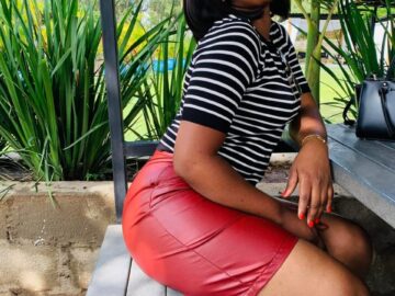 Peris, a sugar mummy in Rongai, seated outdoors on a wooden bench in a striped top and red skirt