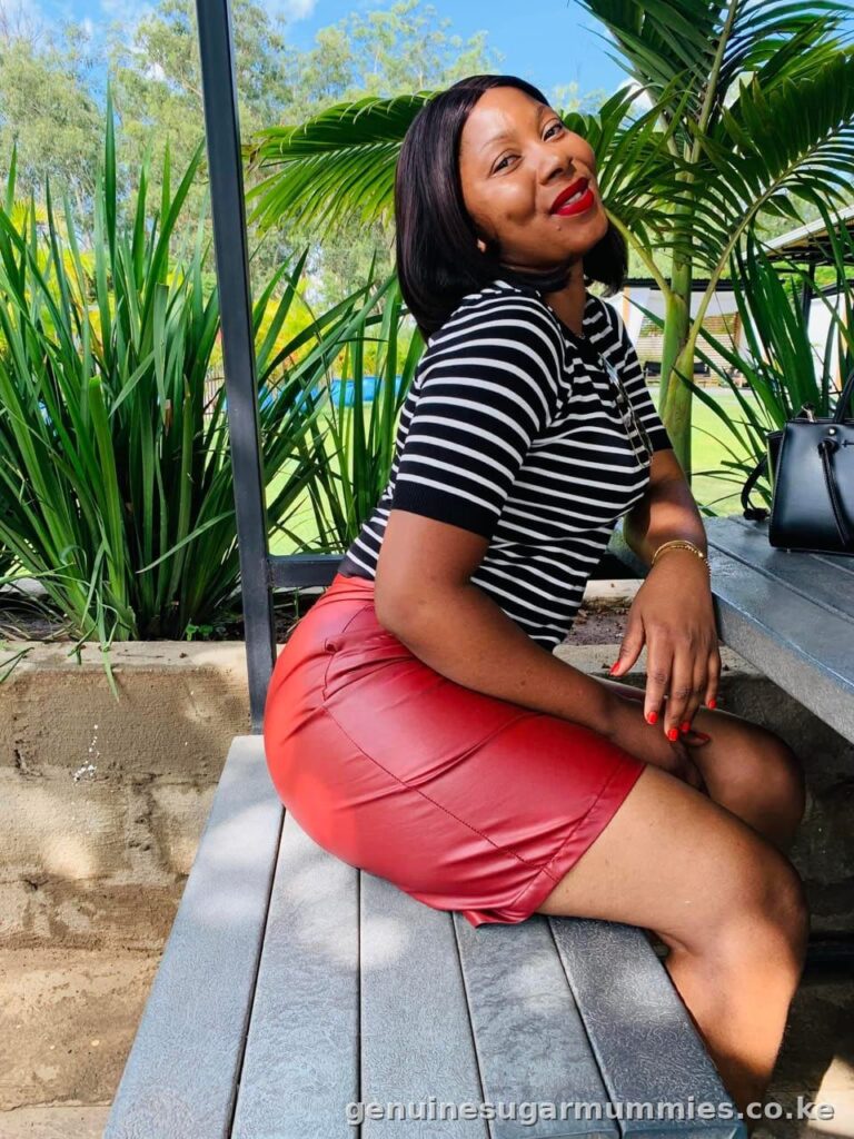 Peris, a sugar mummy in Rongai, seated outdoors on a wooden bench in a striped top and red skirt