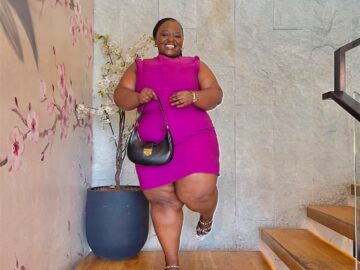 Smiling Nairobi West sugar mummy in a bright pink dress holding a black handbag indoors